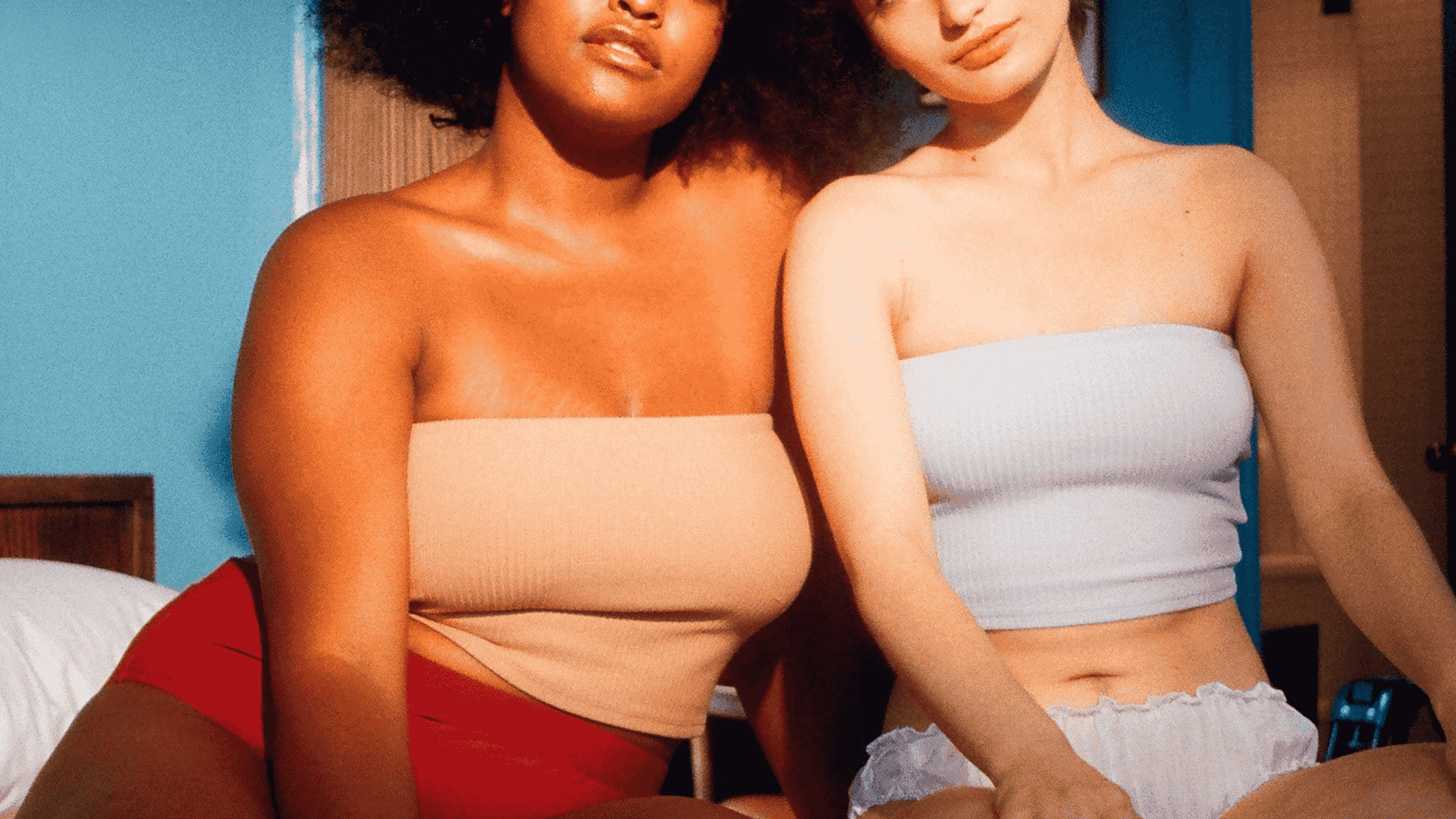 Two femmes in crop tops and briefs sitting confidently together.