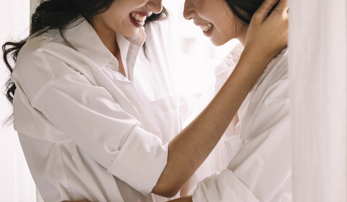 Two women in white shirts smiling and touching intimately, sharing a tender sapphic moment