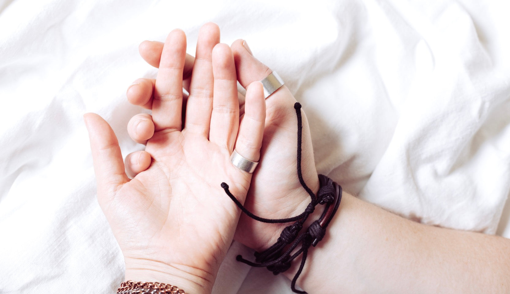 Two intertwined hands resting on white sheets, symbolizing queer connection and shared pleasure